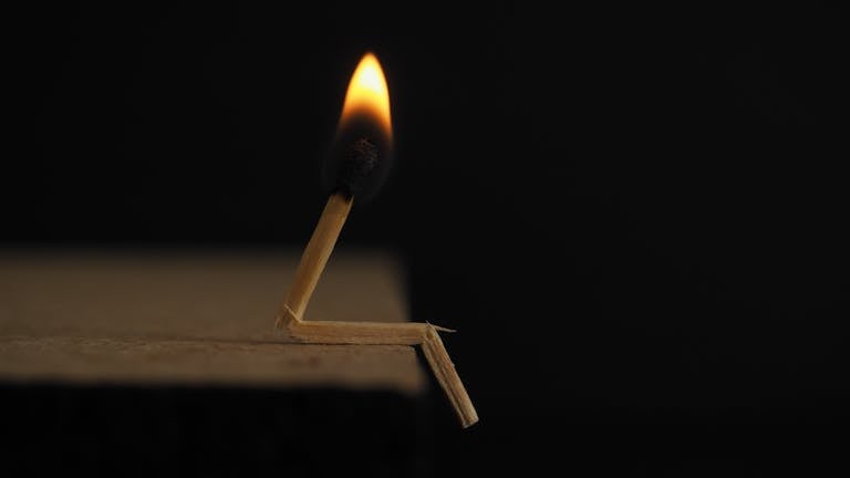 A creative capture of a bent matchstick with a burning flame against a dark backdrop.