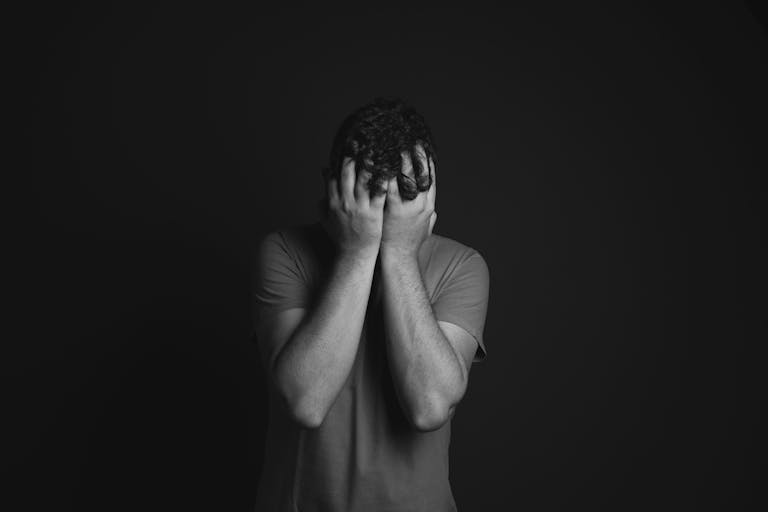 A grayscale portrait of a man covering his face, depicting emotion and mental health themes.