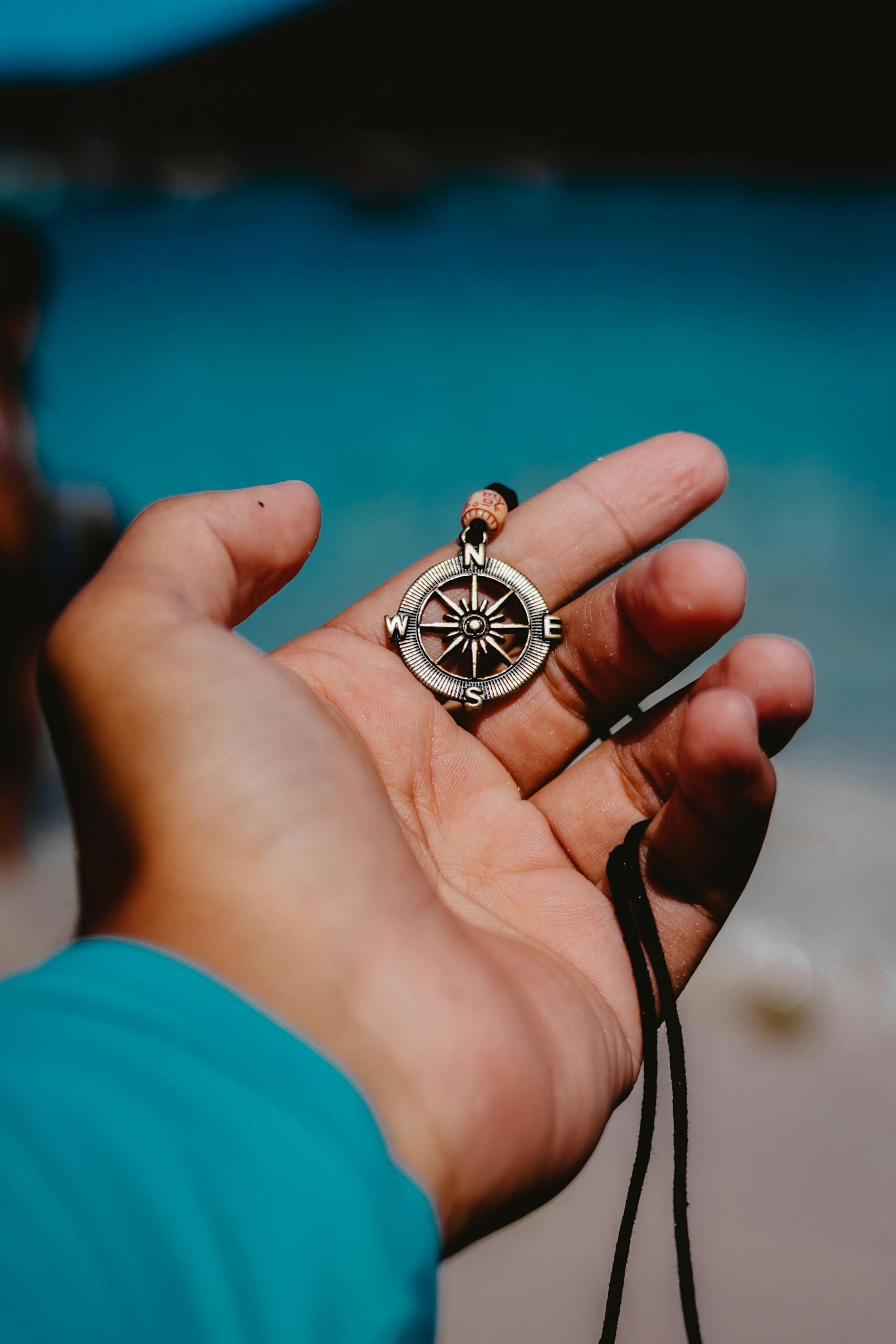 A hand holding a compass pendant with a blurred beach background.