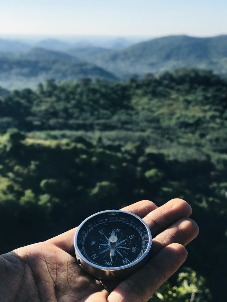 A handheld compass over majestic green mountains under blue skies, ideal for travel themes.