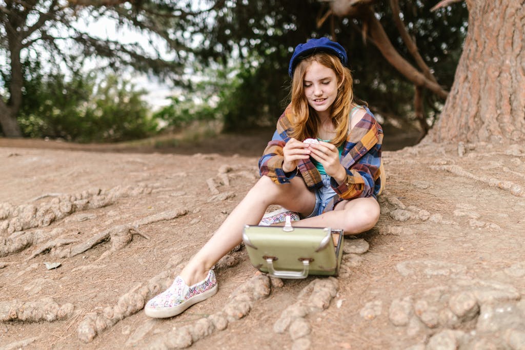 A teenage girl sitting on tree roots, enjoying a book in a natural setting with her backpack.