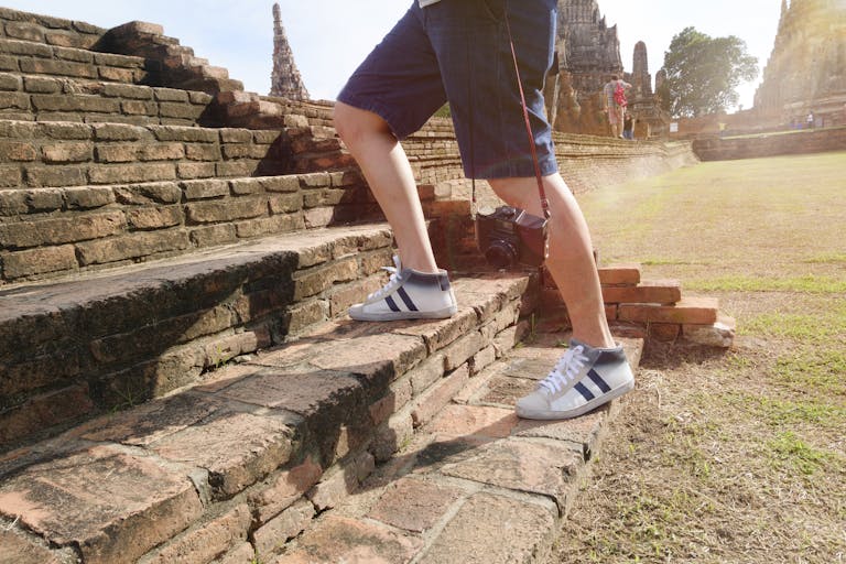 A tourist wearing sneakers climbs ancient brick steps at a historic temple site on a sunny day.