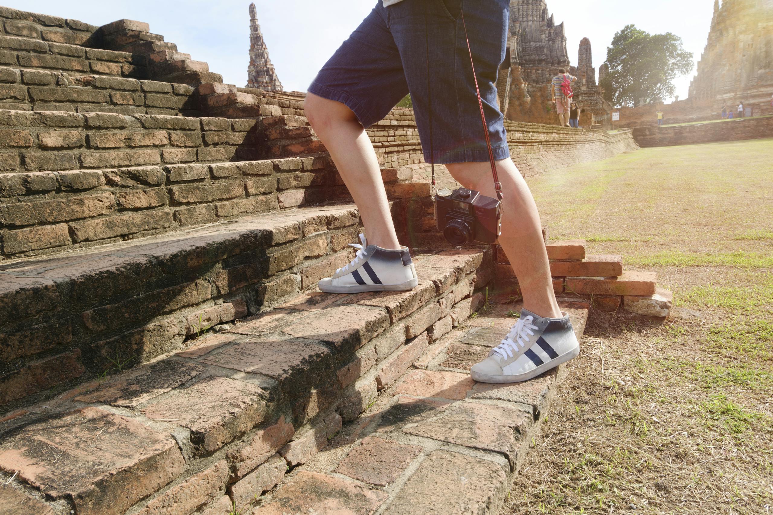 A tourist wearing sneakers climbs ancient brick steps at a historic temple site on a sunny day.