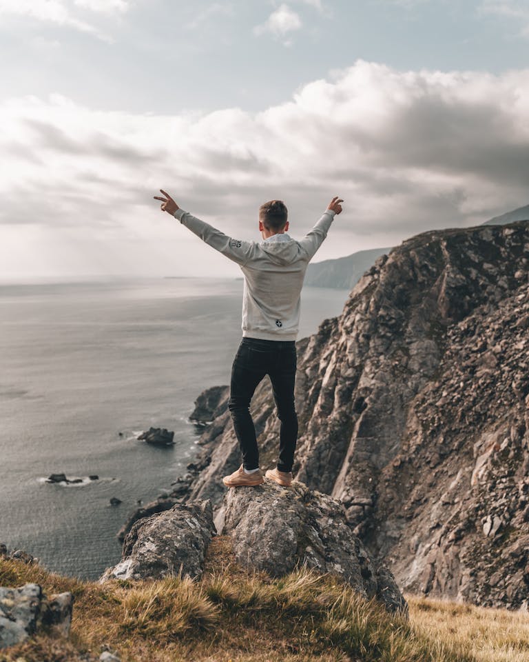 Man enjoys breathtaking view from rocky cliff along Ireland's rugged coastline, embracing nature.