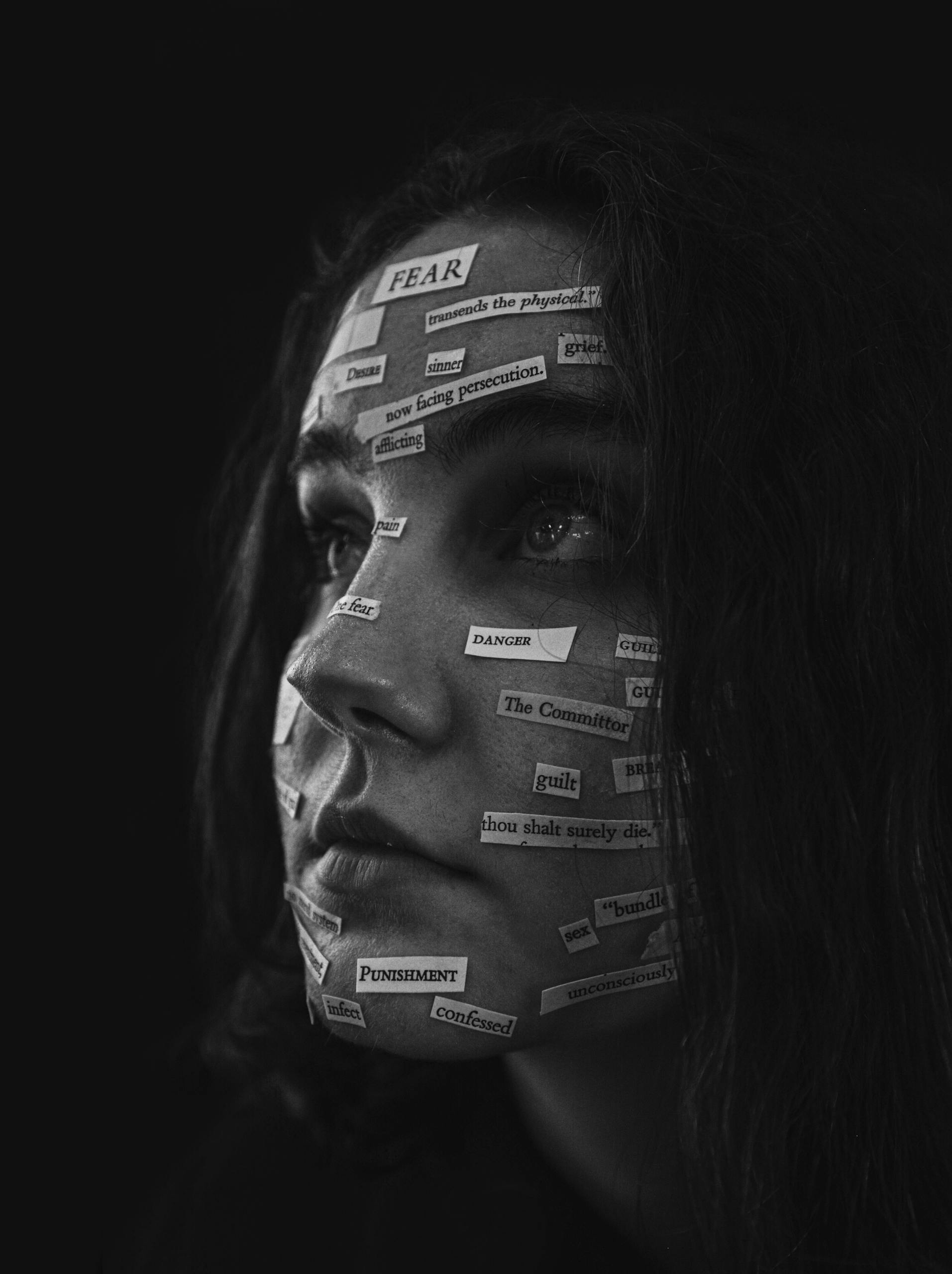 Black and white portrait highlighting powerful emotions with paper cutout text on woman's face.