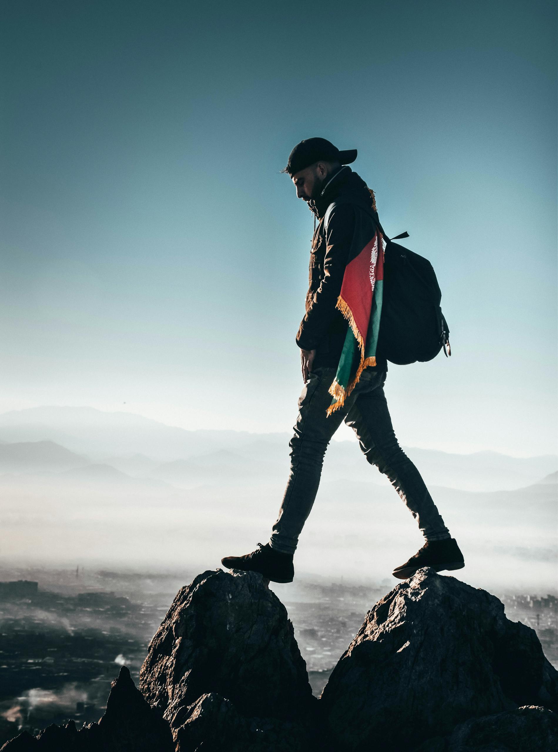 A solitary hiker with a backpack and flag walking atop rocks in the Afghan mountains.