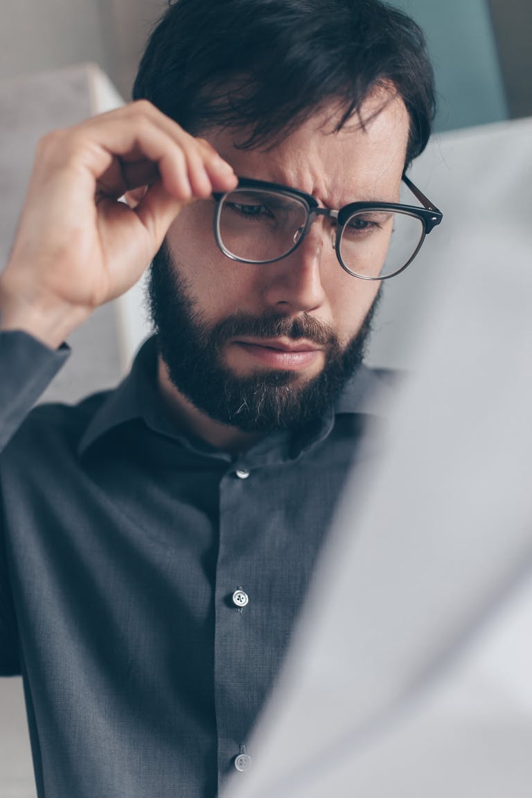 Bearded man in eyeglasses seriously analyzing a document indoors.