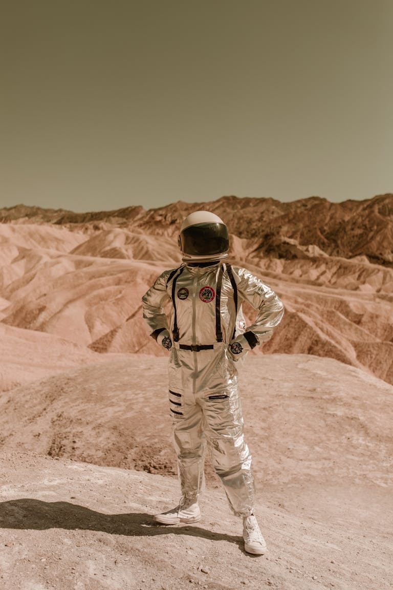 A person in a space suit stands confidently in a barren, desert-like landscape, evoking exploration of distant planets.