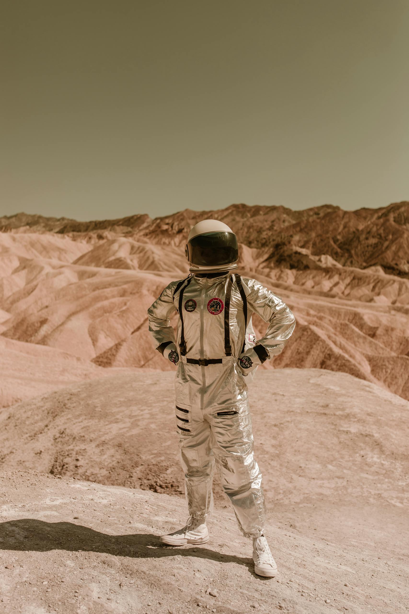 A person in a space suit stands confidently in a barren, desert-like landscape, evoking exploration of distant planets.