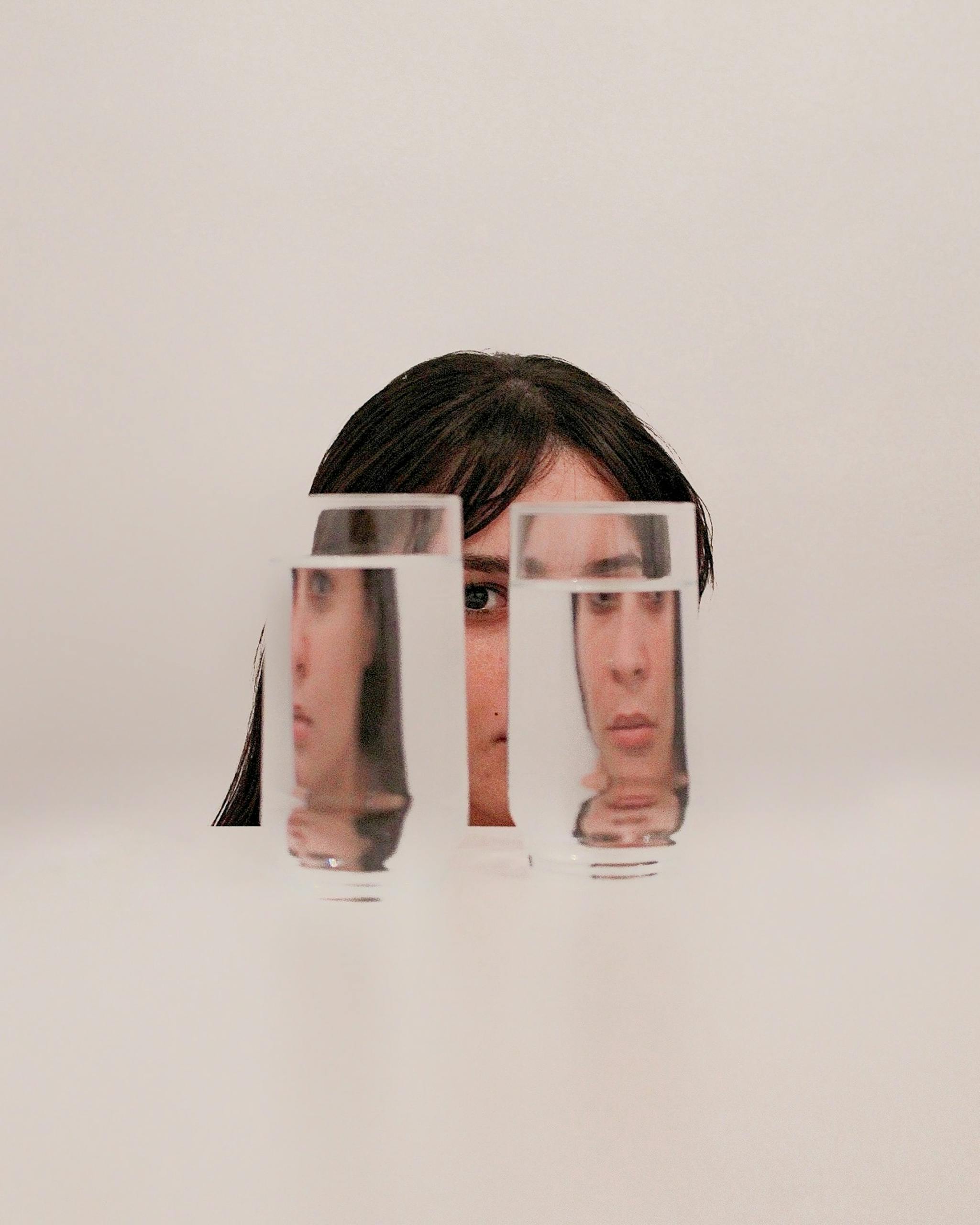 Surreal portrait of a woman with her face reflected through glasses of water, creating intriguing visual distortion.